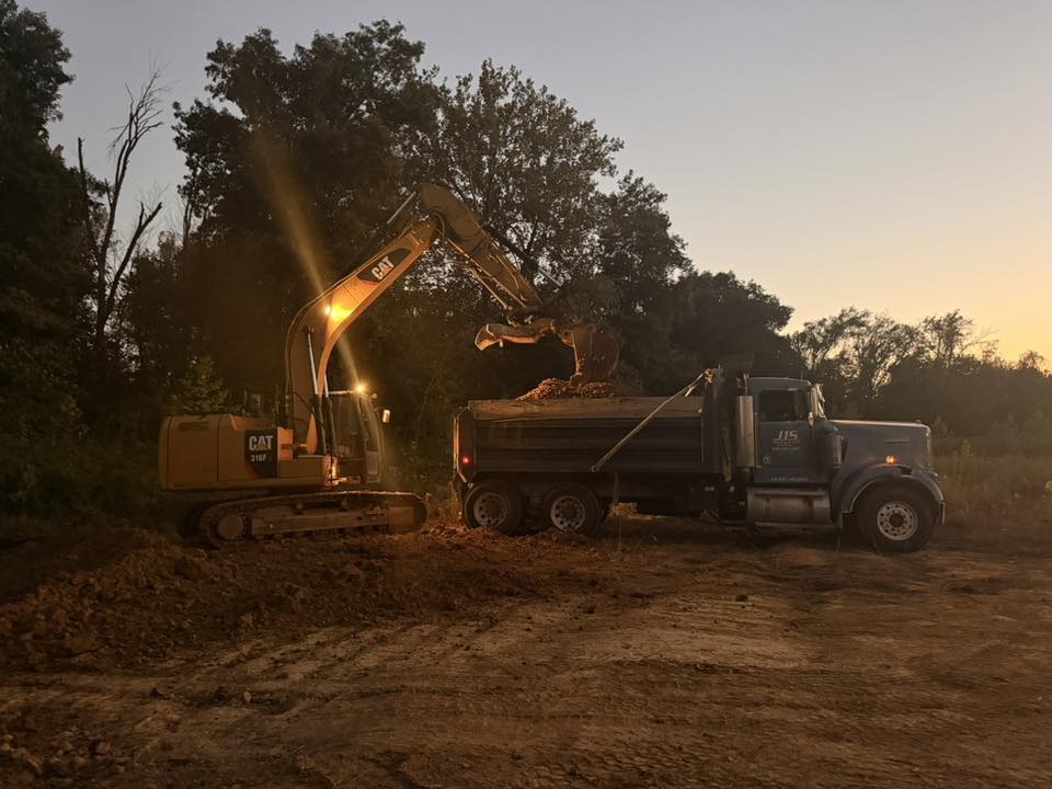 A J1S excavator loading a J1S dump truck at dusk