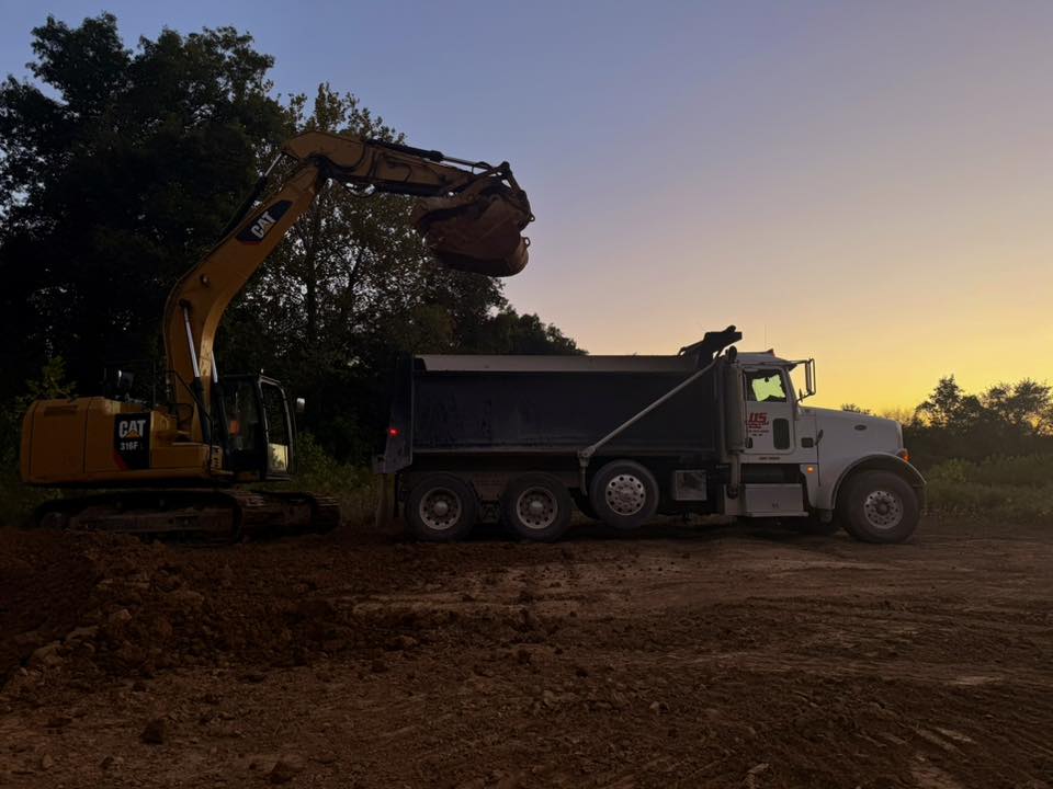 An excavator and a dump truck on a graded lot at sunset