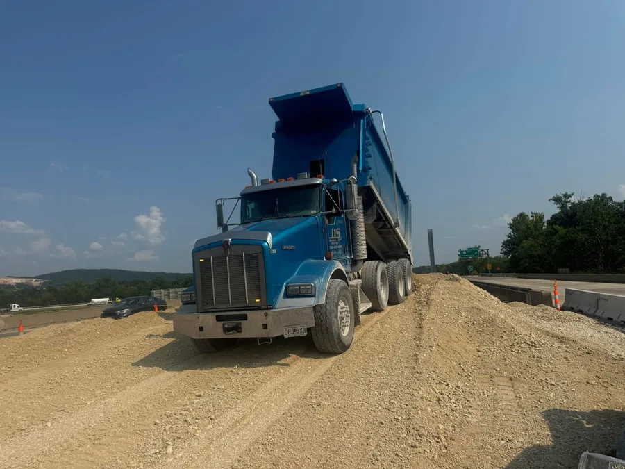 A blue dump truck with its bed raised on a fresh gravel base