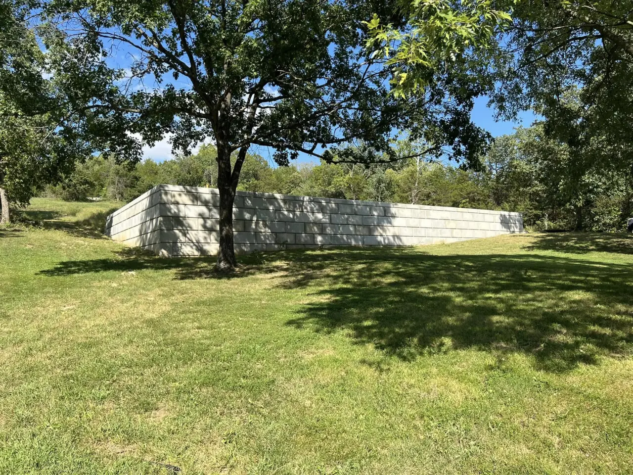 A wall of stacked concrete blocks along the edge of a grassy yard