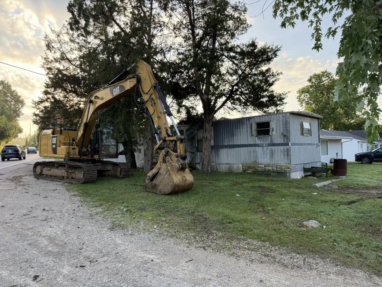 An excavator beside a mobile home before demolition