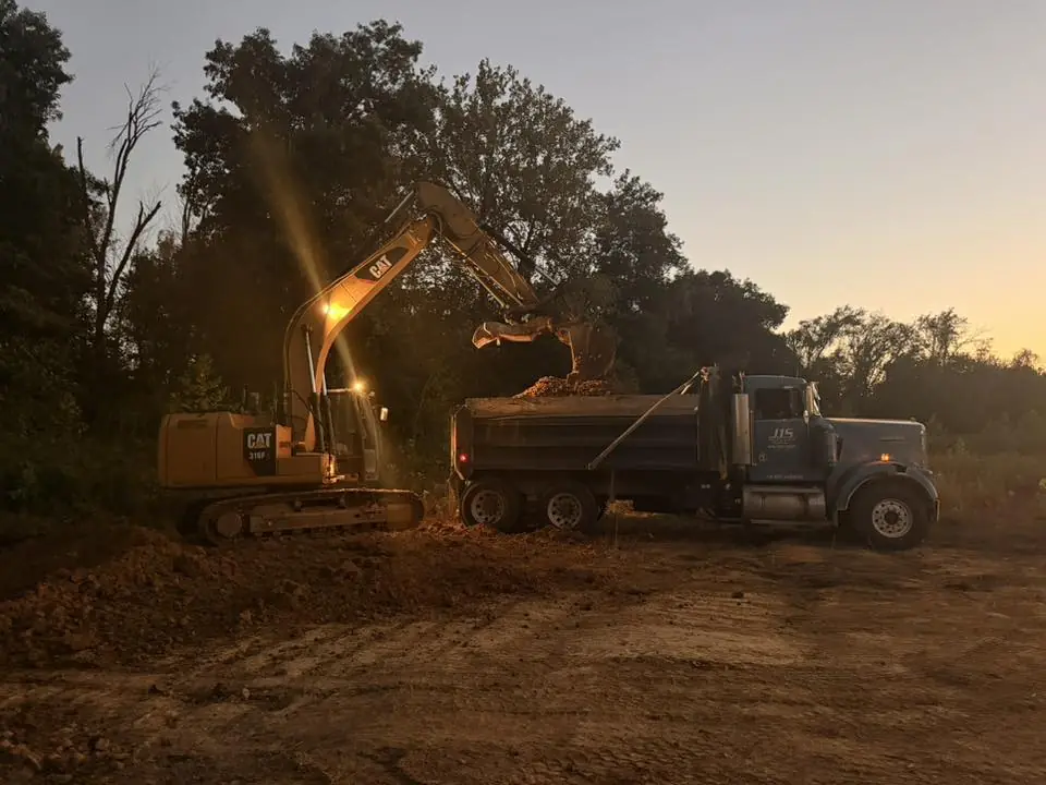An excavator loading a dump truck at dusk with its work light on