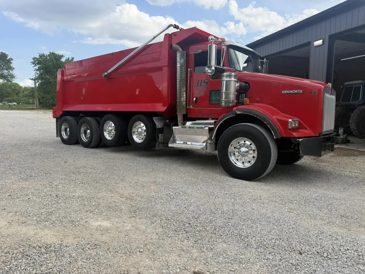 A red quad-axle dump truck parked on a gravel lot