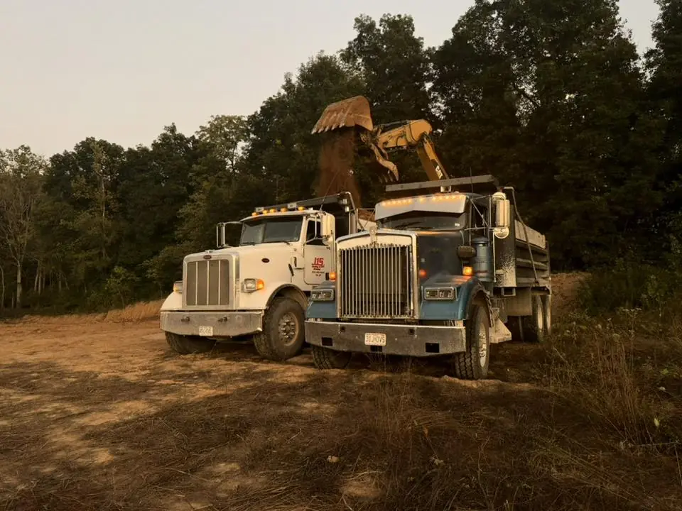 Two dump trucks parked on bare dirt while an excavator works behind them