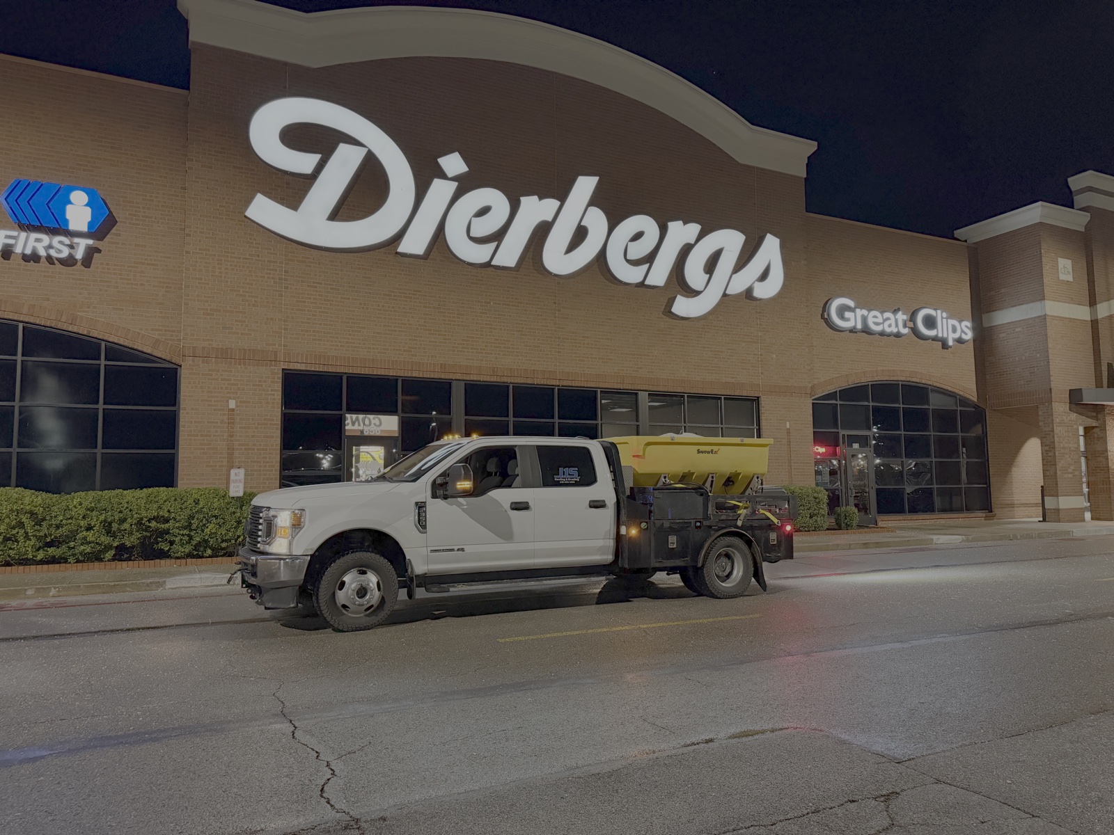 A pickup with a salt spreader outside a Dierbergs store at night