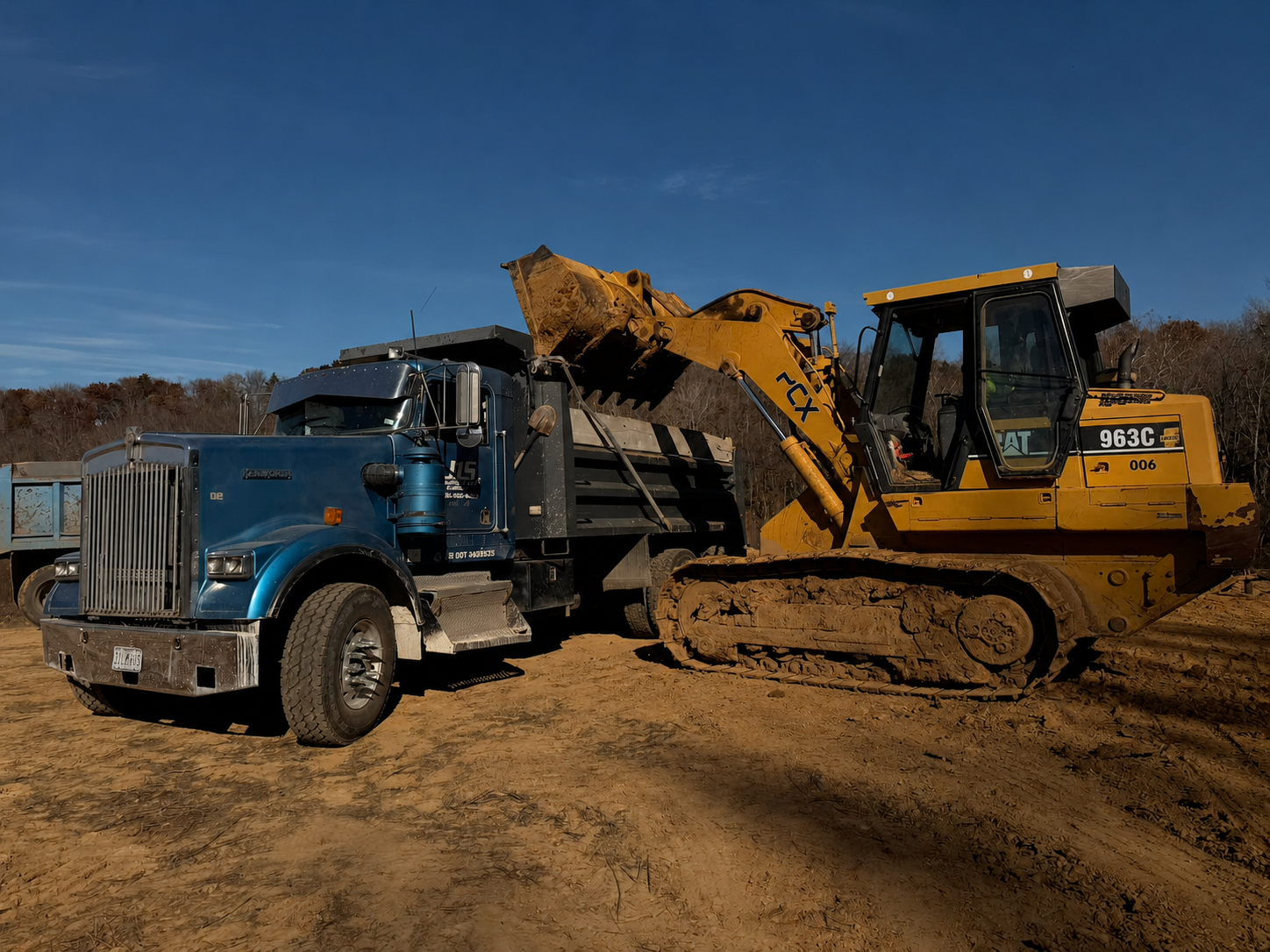 A track loader filling a blue dump truck