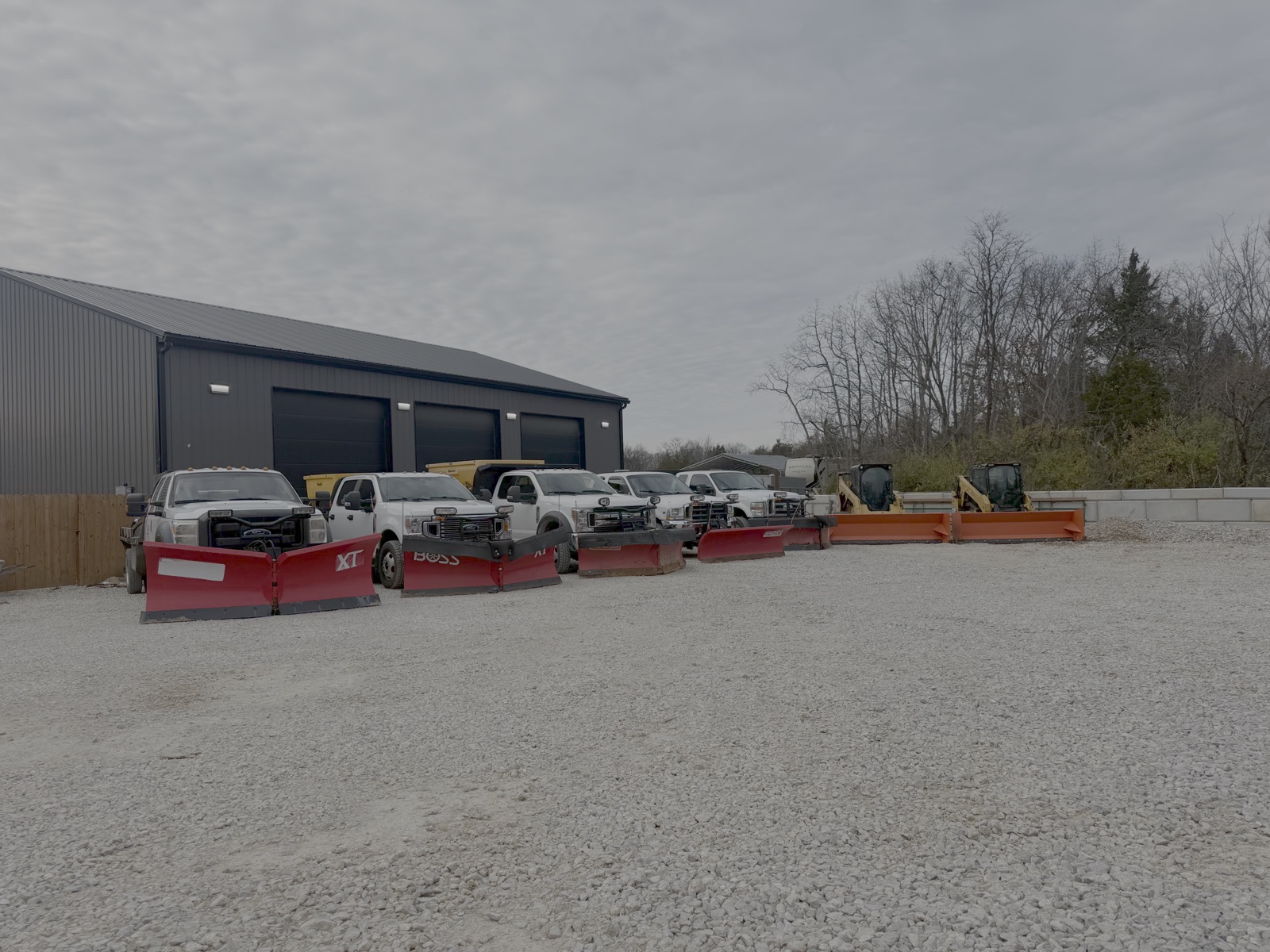 Plow trucks and snow pushers lined up outside a garage