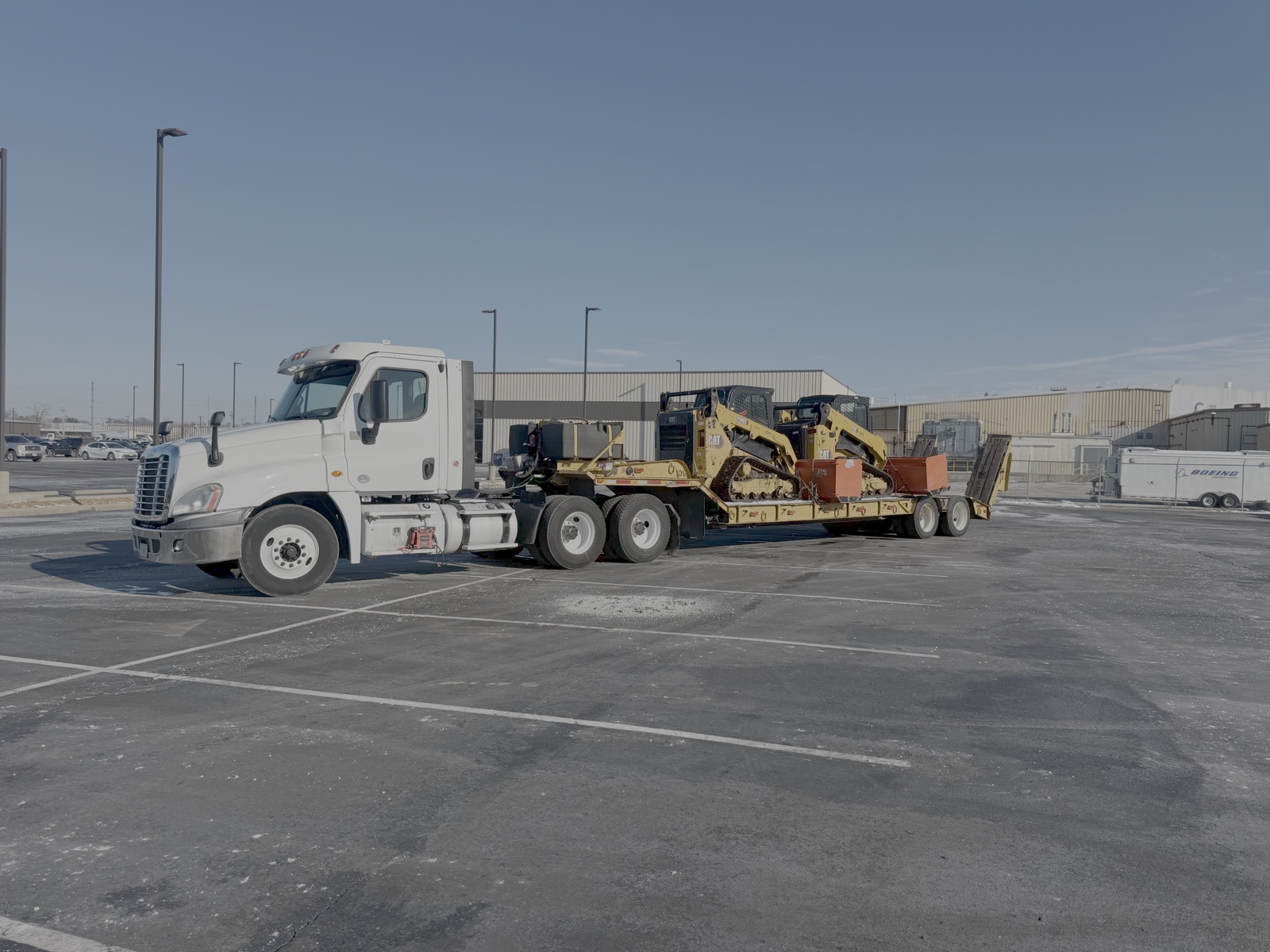 A semi hauling skid steers with snow pushers on a trailer